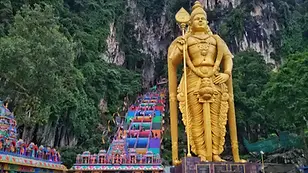 Golden Lord Murugan statue at Batu Caves with colorful staircase leading into limestone caves.
