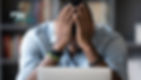 Man at laptop with head in hands, looking stressed; rw networks logo in corner, blurred bookshelves behind.