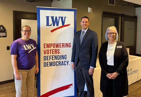 Lyn and Kate standing with Michael Howe beside an LWV banner at a naturalization ceremony.