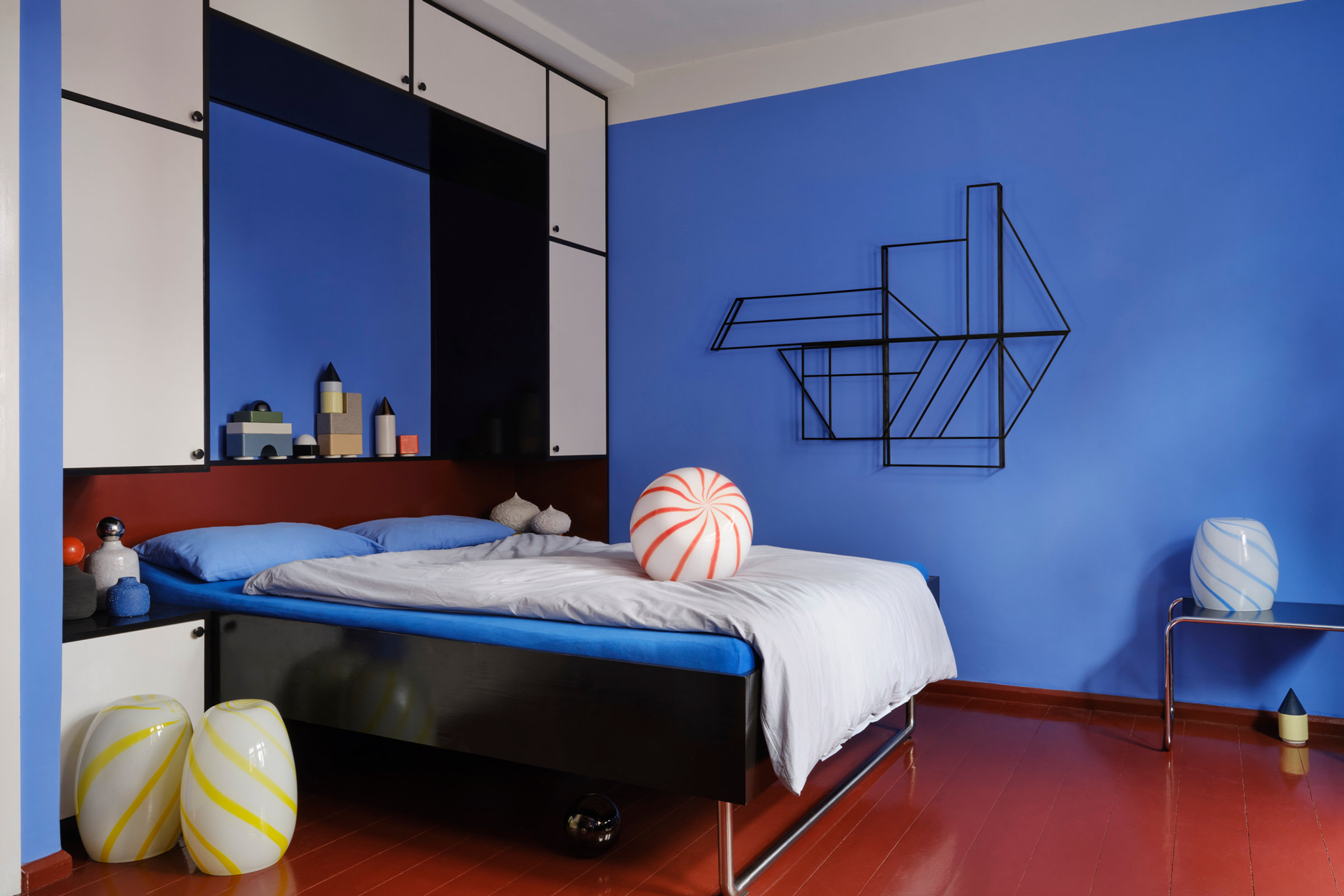 STUDIO BERG objects in a blue bedroom at Tautes Heim, Berlin: FOLDWORK on the wall, KNSTRKT on the shelf and a striped CANDY object on the bed