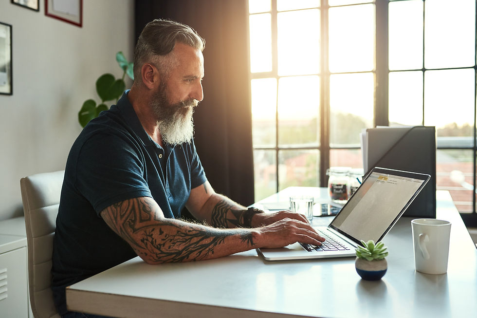 A man sits at a desk in front of his laptop, waiting to join a telemedicine telehealth appointment in the light of morning.