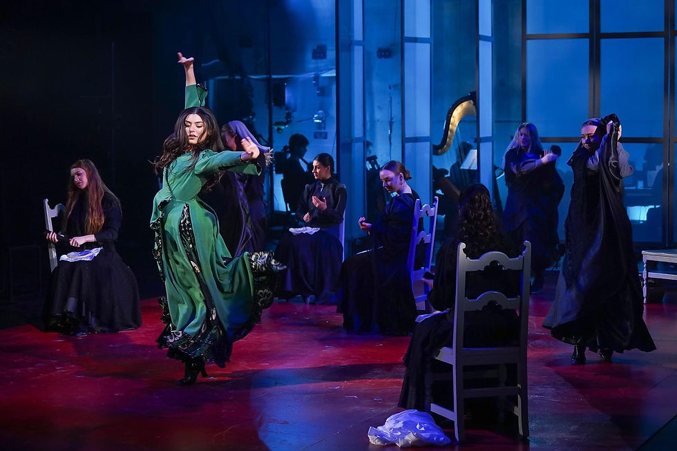 Dancer in green wrap dress on a red stage floor surrounded by a company of women in black