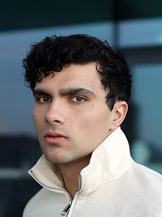 Troy - headshot of male model with curly hair, a clean-shaven face, and wearing an T-shirt with a tennis racket behind his head, represented by ROC Talent Agency UK