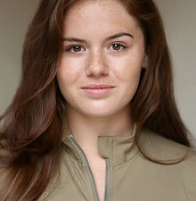 Demi C - headshot of a female actor with long red curly hair, brown eyes, and wearing a green zip up, represented by ROC Talent Agency UK