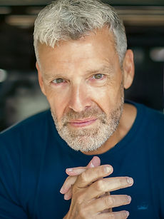 Adrian - A headshot of a classic model with short hair, stubble, and a blue t-shirt, represented by Roc Talent Agency UK