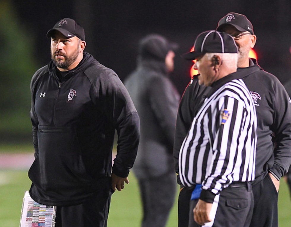 Sports photography showing a football coach interacting with officials on the sidelines. The mood is focused and serious during a night game.