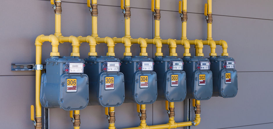 Row of residential natural gas meters and yellow pipe plumbing on exterior wall to measure