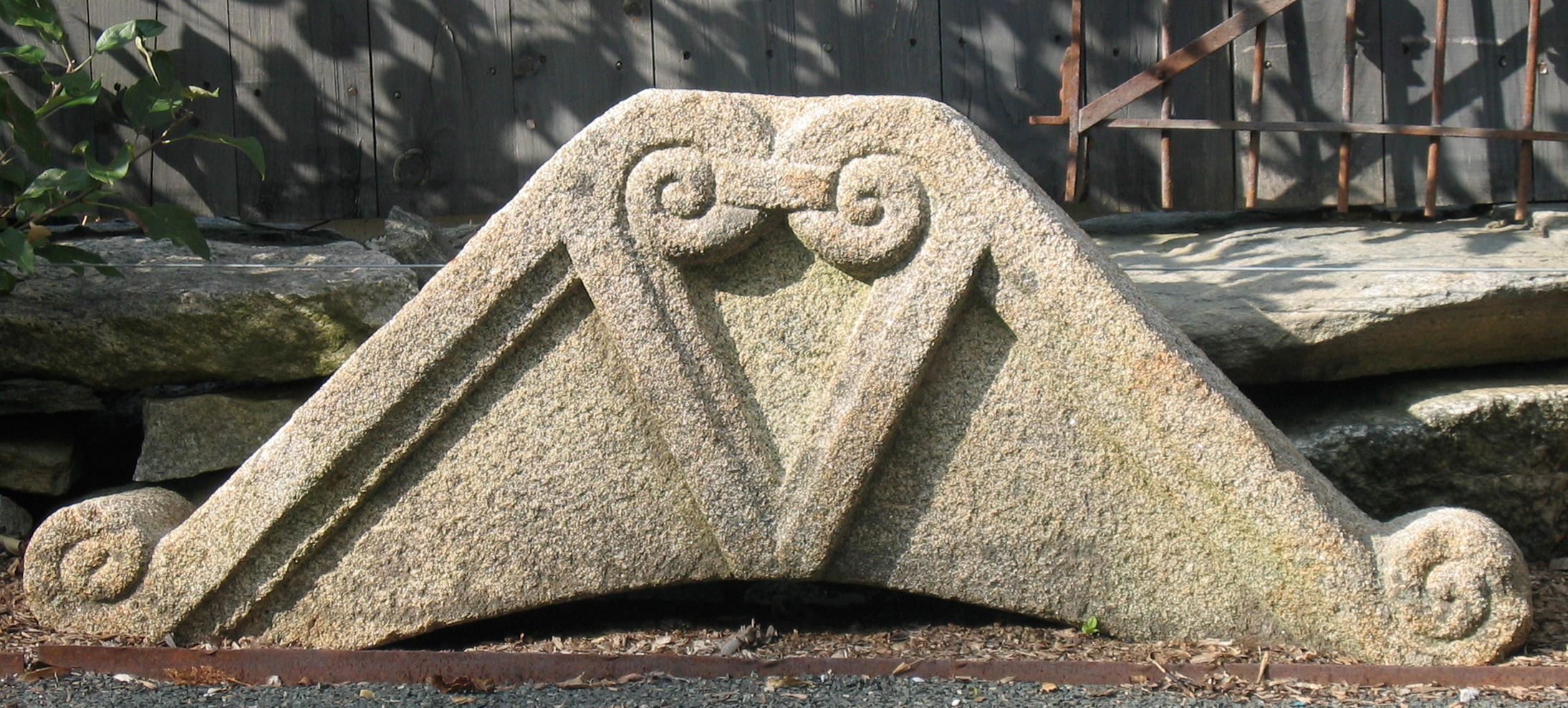 18th‑century French granite pediment with classical triangular profile in a garden setting.