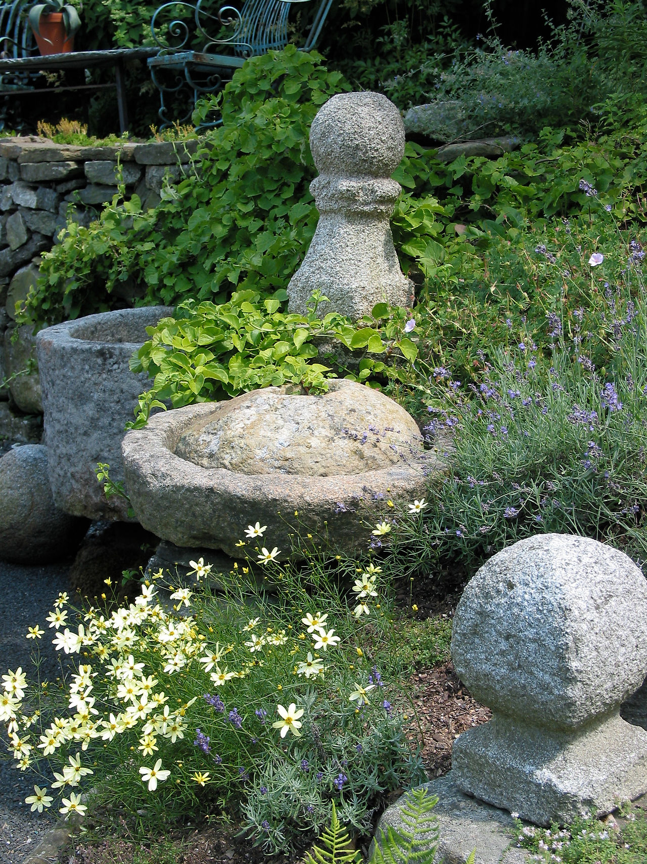 Antique closed granite mill and finials displayed in natural garden setting.