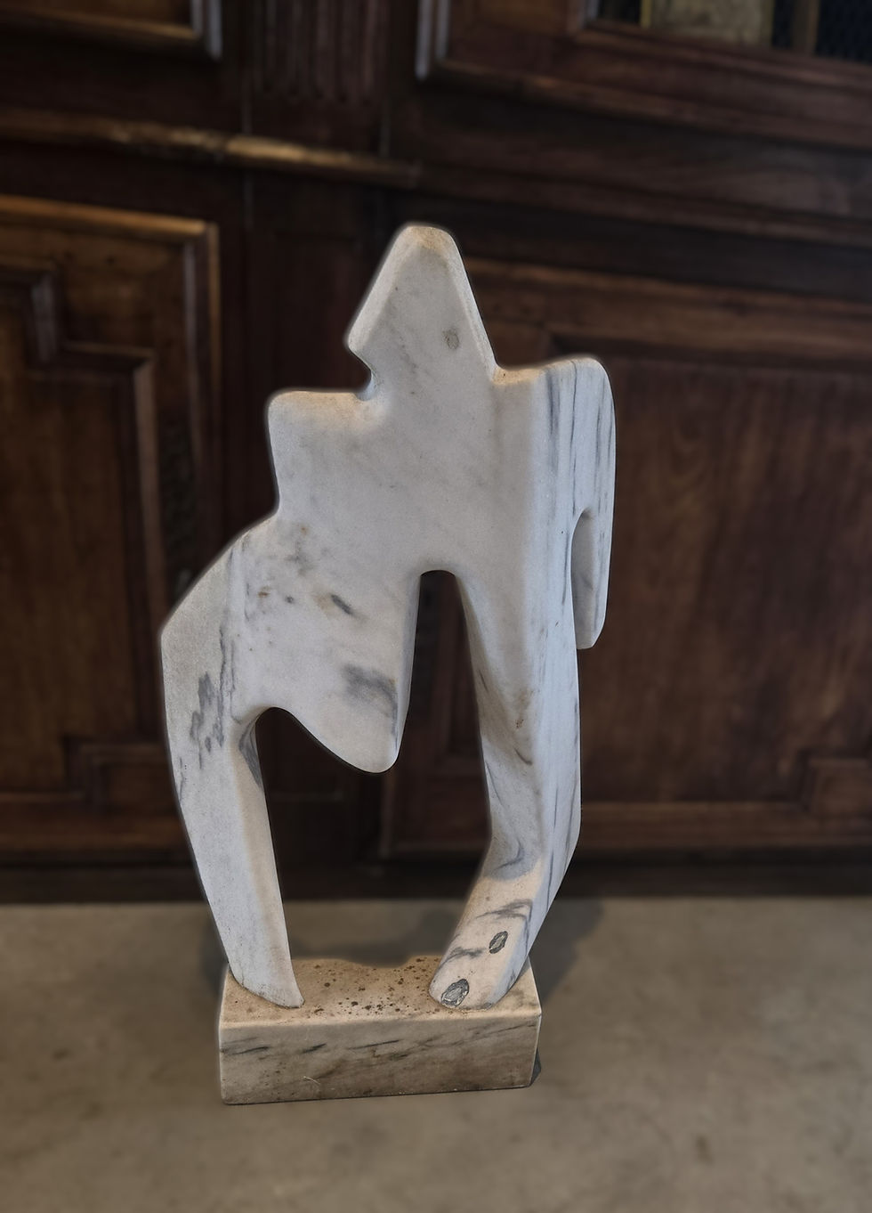White abstract sculpture, Abstract Marble Sculpture, against a dark wooden cabinet.