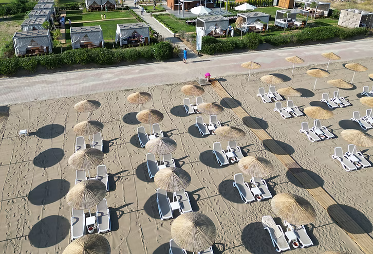 Ein weitläufiger Strand mit weißen Liegestühlen und Strohschirmen am Meer – der perfekte Ort zum Entspannen und Sonnenbaden.