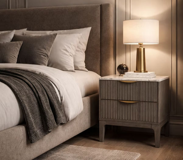 Cozy neutral bedroom with a upholstered bed, layered pillows, gray throw, nightstand lamp, and books in warm soft light