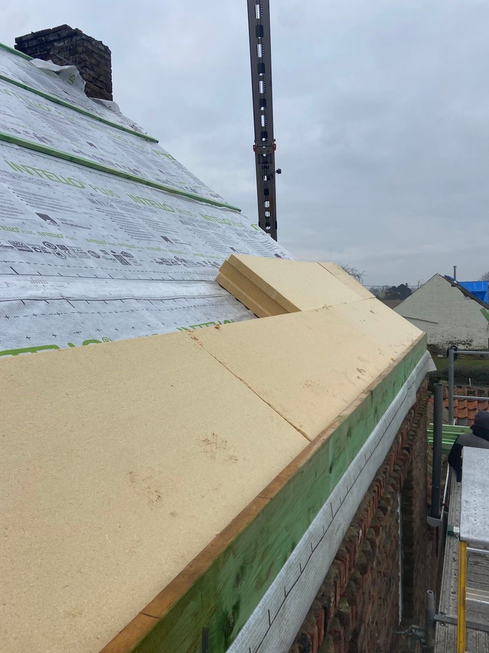 Travaux d’isolation de toiture avec pose de panneaux isolants rigides sur pare-pluie Intello, charpente apparente en cours de