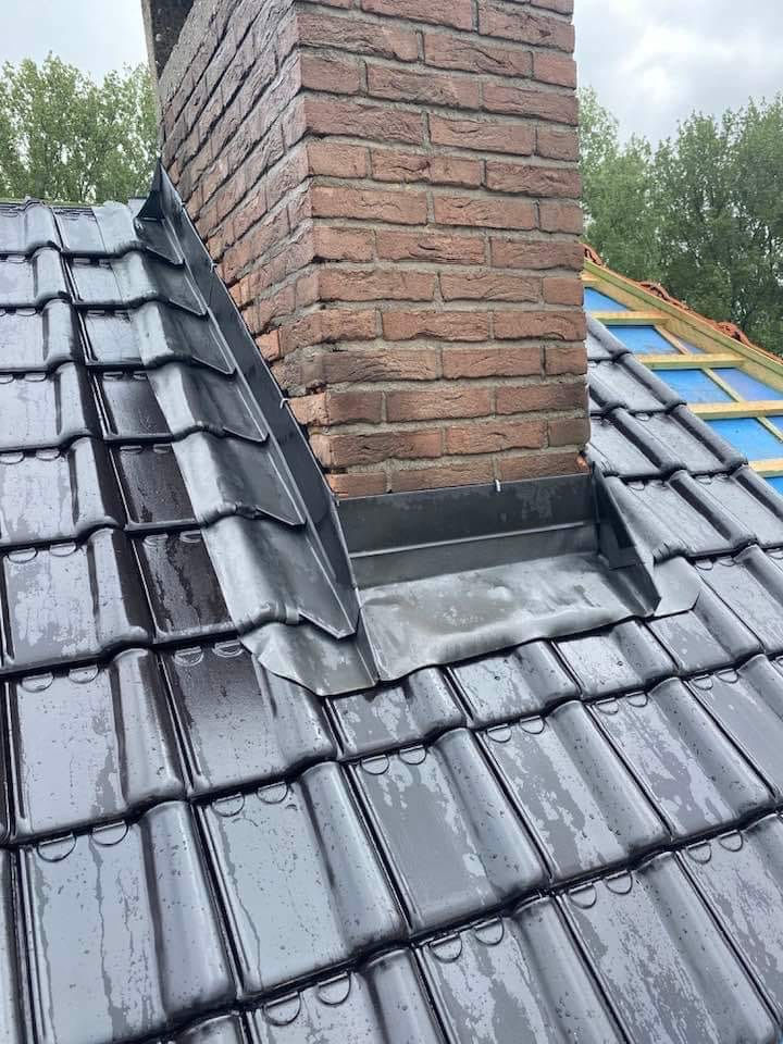 Détail de finition en zinguerie autour d’une cheminée en briques sur toiture en tuiles anthracite, étanchéité assurée par sol