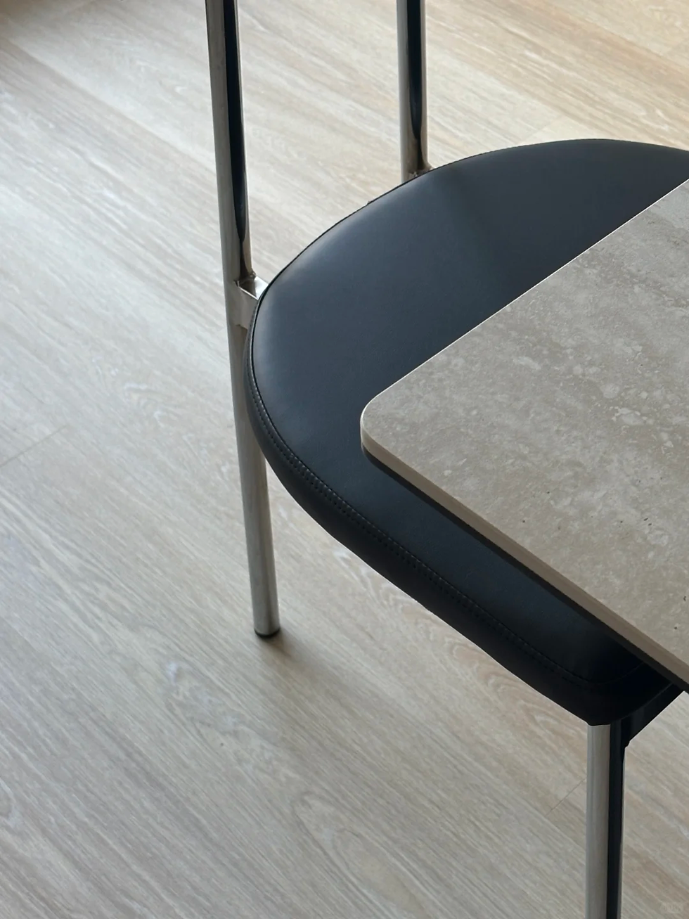 Close-up of a black chair tucked under a stone table on a light wood floor, in a clean, minimalist room.