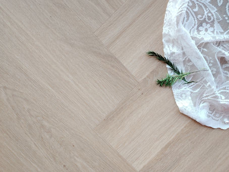 White lace fabric with a small green sprig lies on a light wood parquet floor.