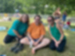 Three middle-aged individuals, two female and one male, sitting together smiling on a hot summer day in the park.