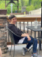 Smiling lady with black hair and silver highlights sitting in a chair with a fountain drink in front of her on a warm day.