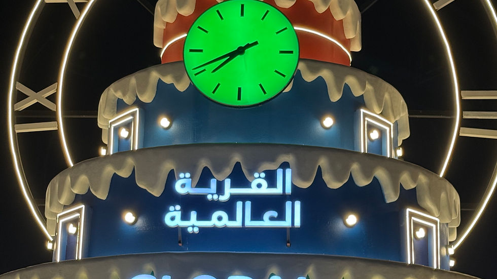 Illuminated structure shaped like a cake with a green clock. Text reads "30 Seasons" and "Global Village" in Arabic and English. Night setting.
