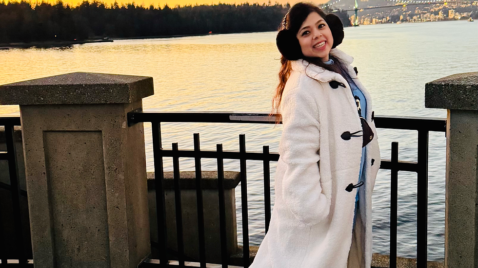 A woman standing against a sunset, wearing a white coat and blue jeans