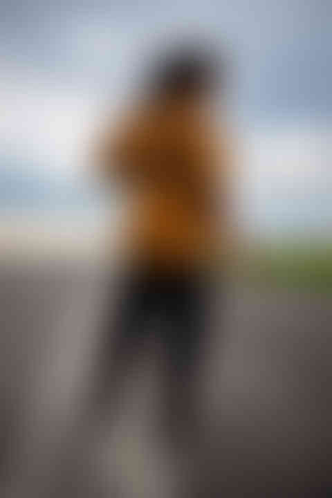 a woman in a brown jacket and black pants is walking down a road