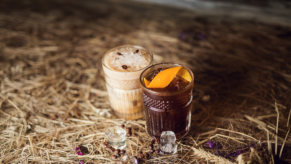 Two garnished, craft cocktails sitting on top of hay in a rustic, Western venue