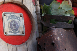 Close-up of a vintage Luckenbach beer emblem mounted on distressed wood with leafy greenery and rusted metal accents.
