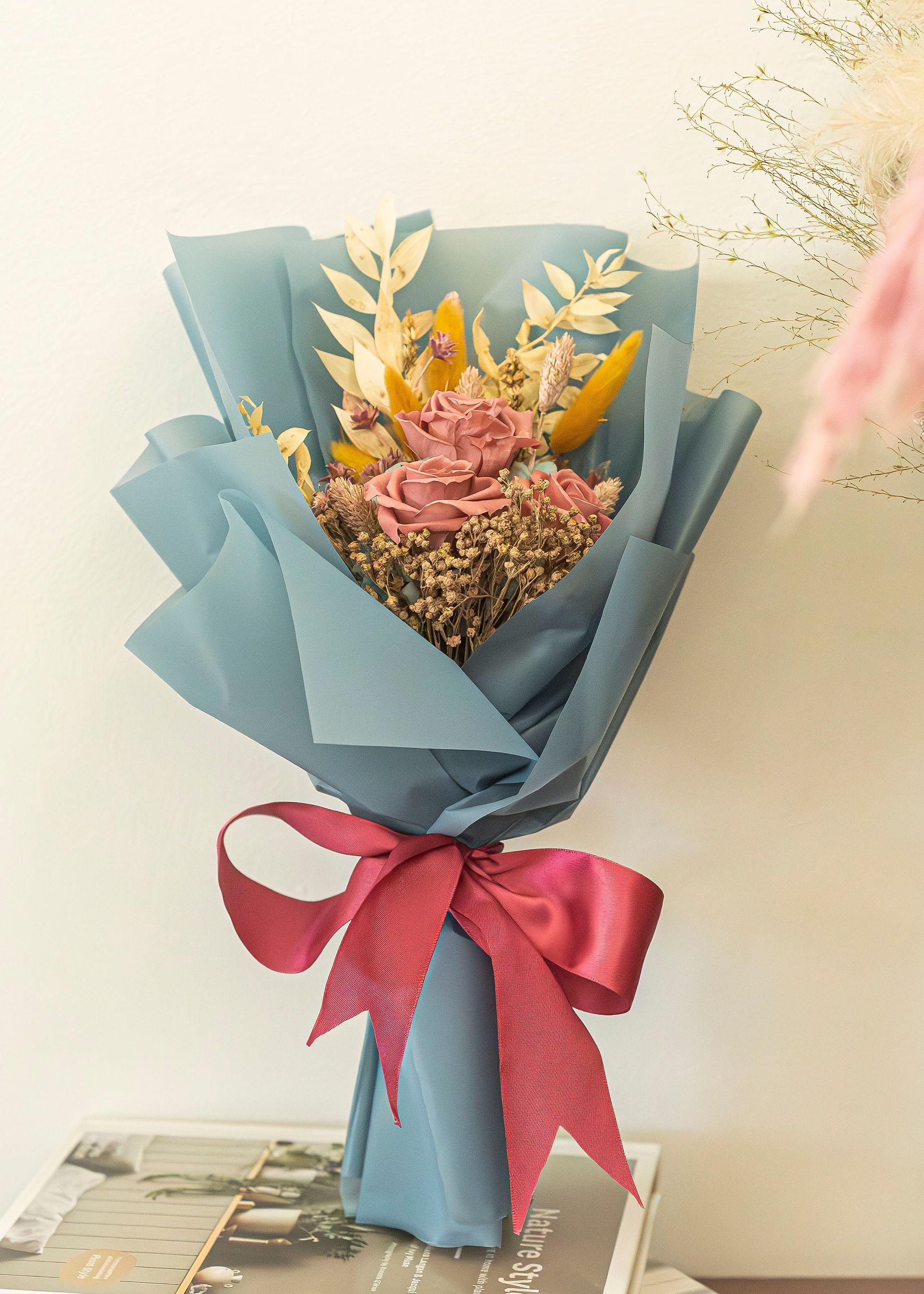 Preserved dusty pink roses with golden dried foliage wrapped in elegant slate teal paper and tied with a burgundy satin ribbon by SKfleur.
