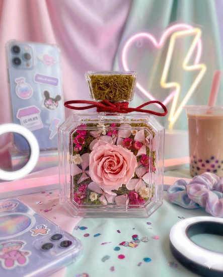 Pink preserved rose in a clear square bottle styled on a trendy desk by SKfleur.