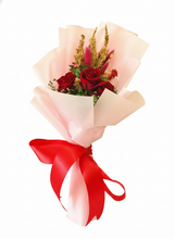 Red preserved roses wrapped in soft blush pink paper with a bright red bow by SKfleur.
