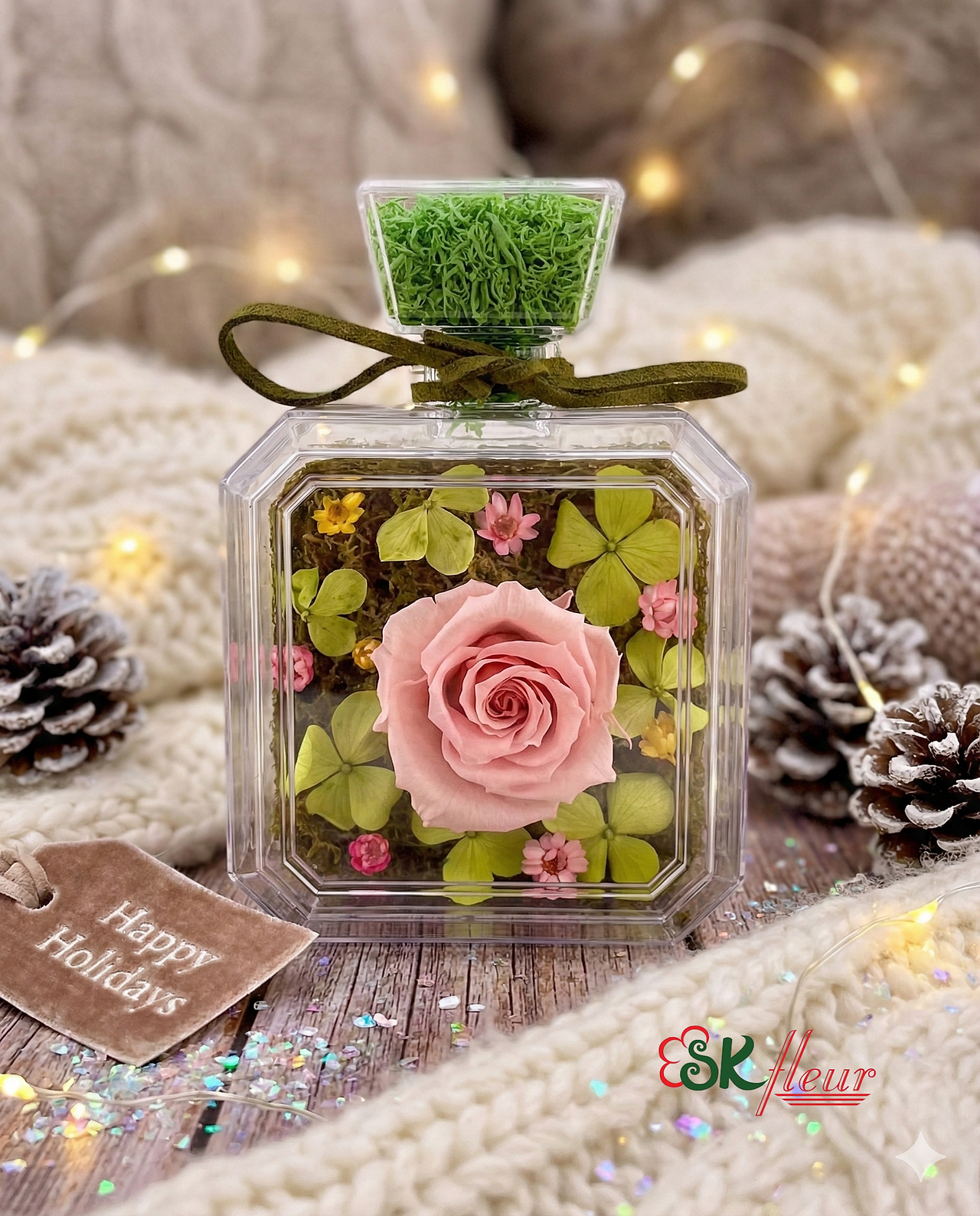 Pink preserved rose surrounded by green hydrangea foliage in a clear square bottle by SKfleur.
