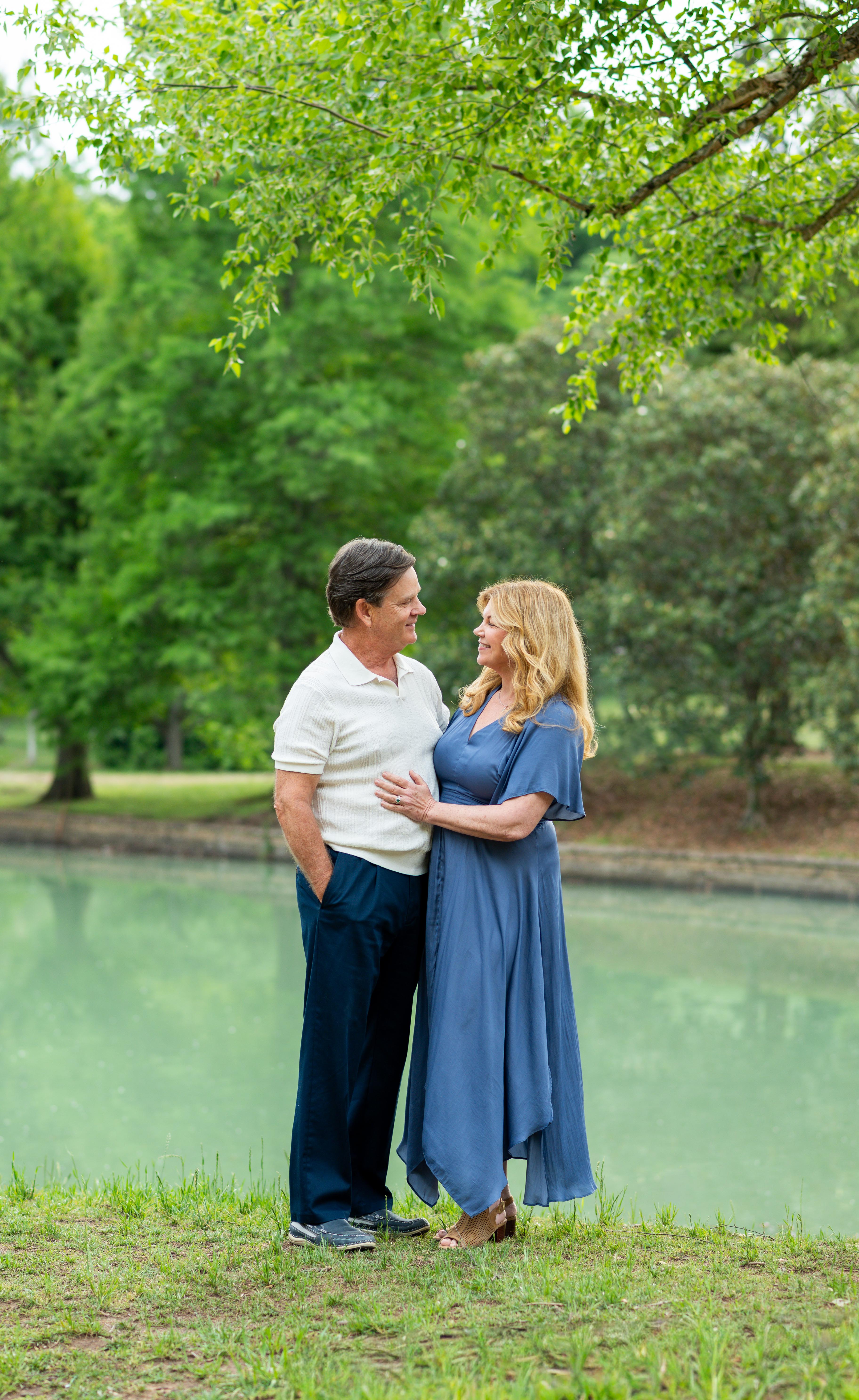 Candid summer photo of Husband and wife smiling at each other beside a beautiful lake. Family photographers in Charlotte, NC. 