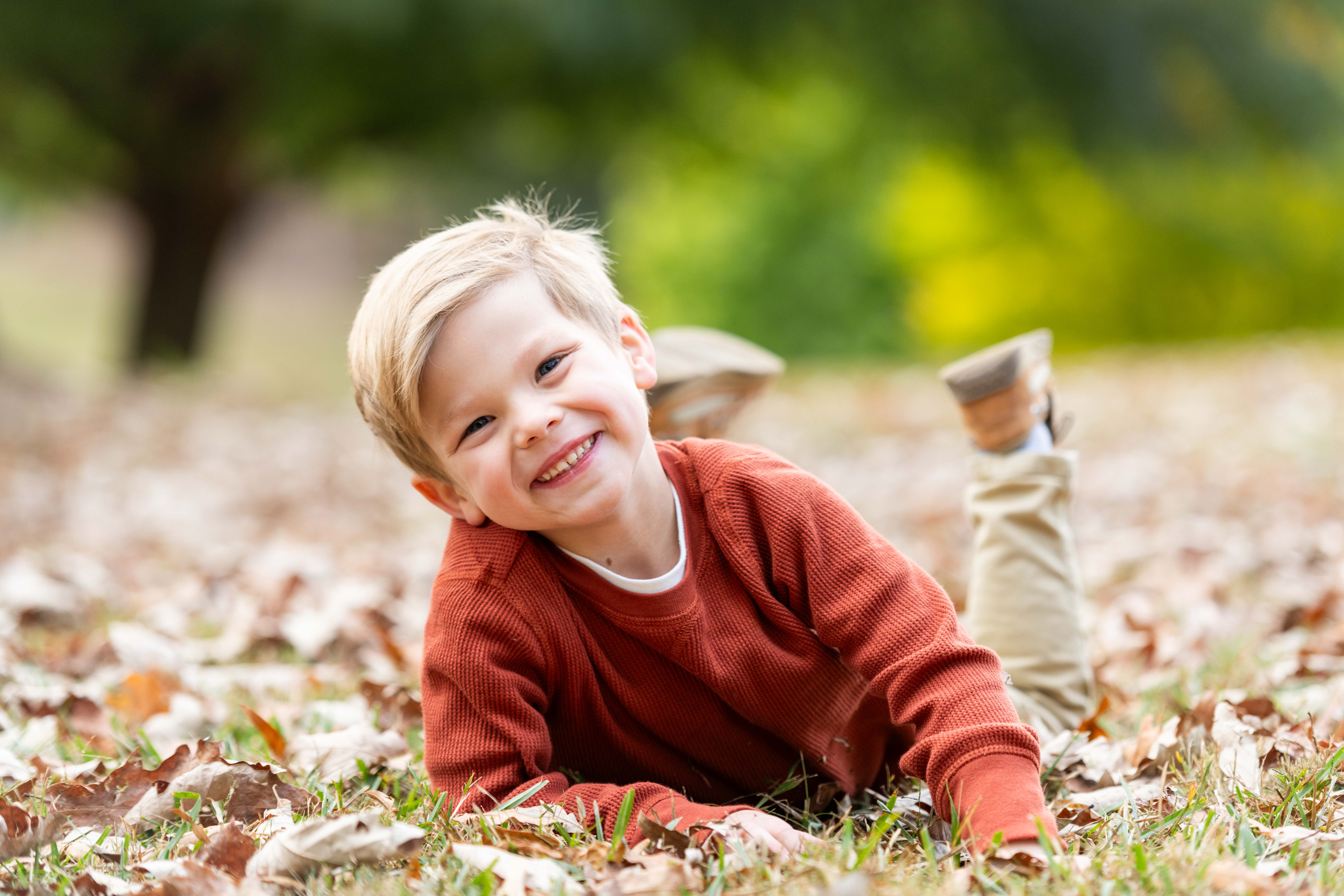 Photo of young boy smiling and laying on his stomach in fall leaves at Freedom Park in Uptown.  Charlotte Family Photographers. 