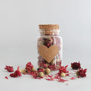 Getrocknete Blüten aus Kornblumen als Streudeko für die Hochzeit. Danaben steht ein Glas mit Korkherz.