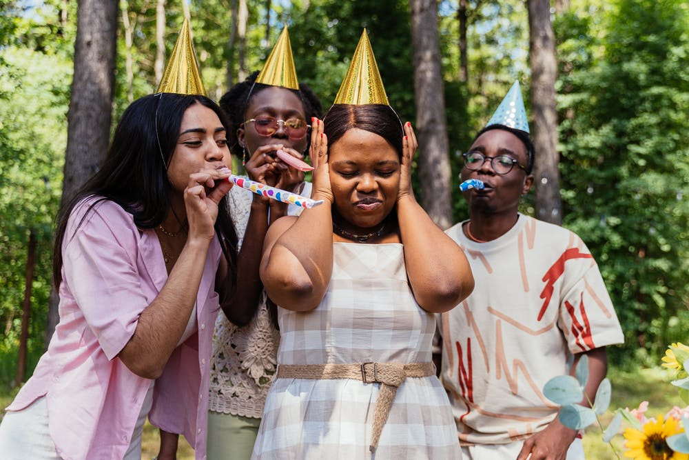 A person covers their ears surrounded by others using party noise makers