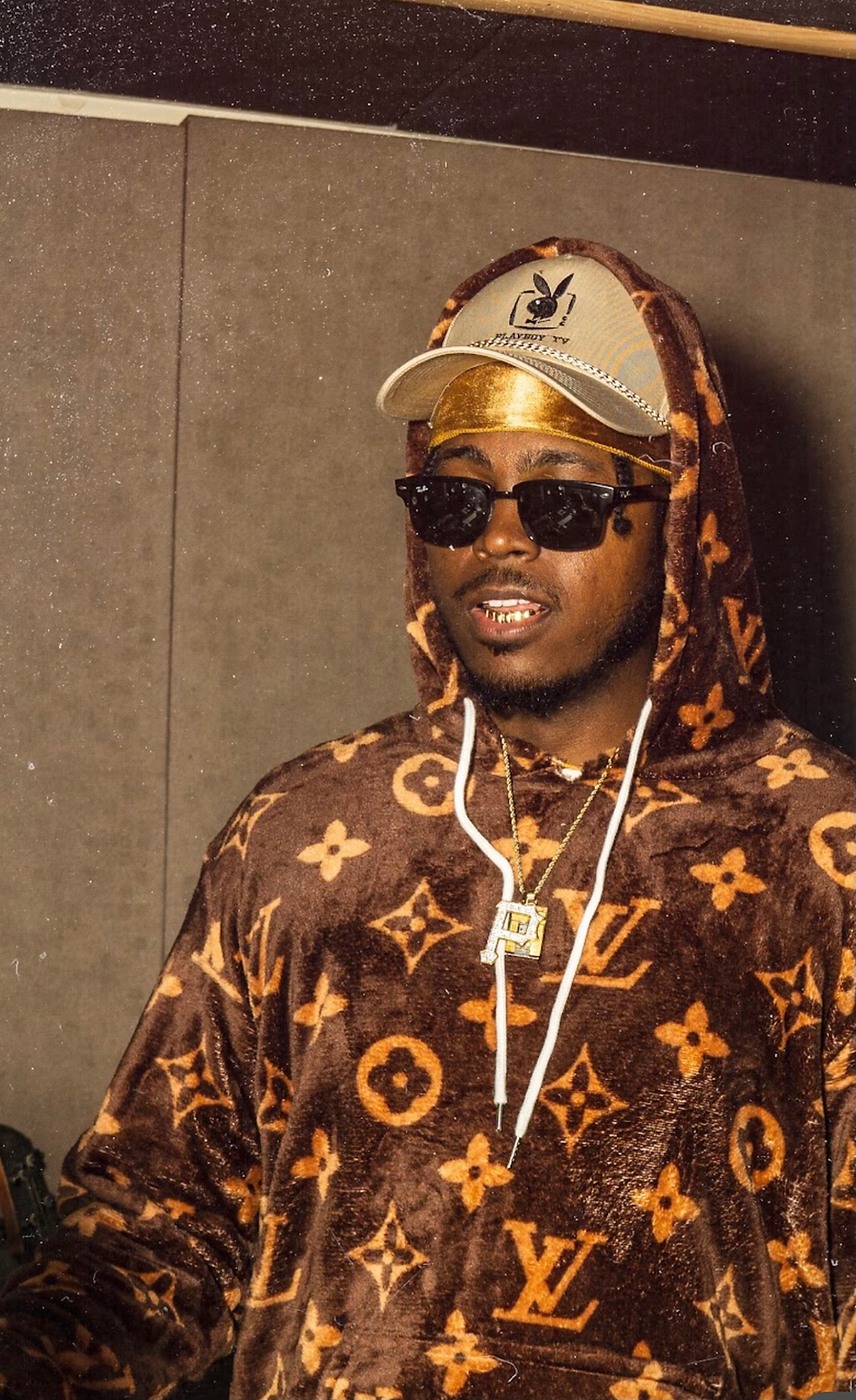 photo of Gho$t! in a brown and gold Louis Vuitton hoodie, tan Playboy hat, gold durag, sunglasses, and a gold Pittsburgh "P" chain