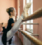 A dancer stretching wth her leg on the barre.