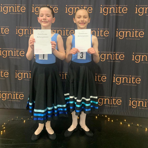 Two young ballet dancers dressed in blue leotards with character skirts and shoes, posing with a certificate