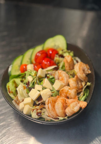 Ein Salat mit Garnelen, Tomaten, Gurken und Käse in einer Schüssel serviert