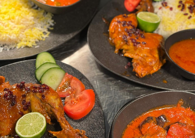 Verschiedene Teller mit Reis, Fleisch, Gemüse und Soße. Auf einem Tisch angerichtet.