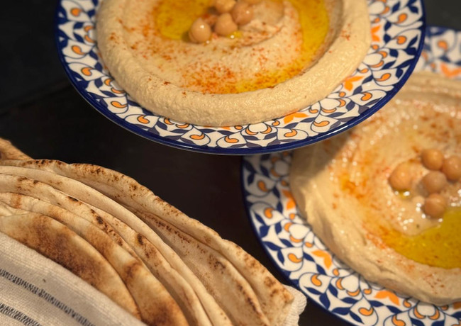 Hummus mit chickpeas, pita bread, and oil on decorative plates for serving.