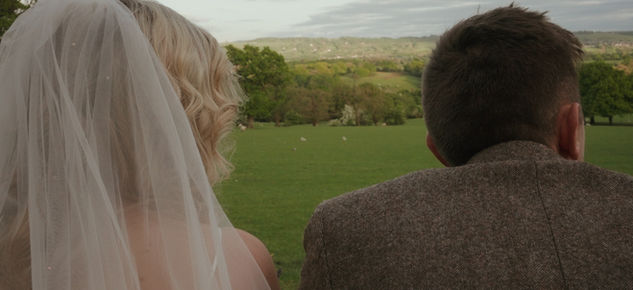 Bride in veil and groom in tweed jacket admire green landscape at Shireburn Arms.