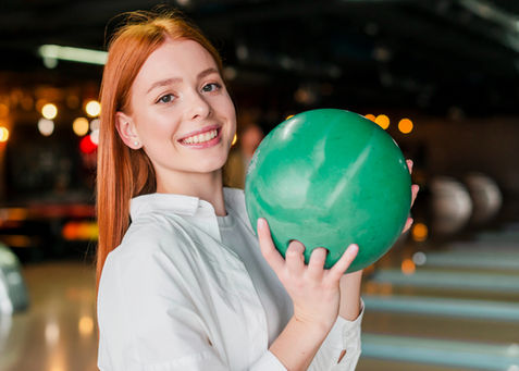 Smiling woman in white holding green bowling ball at Level Up Bowl & Bistro