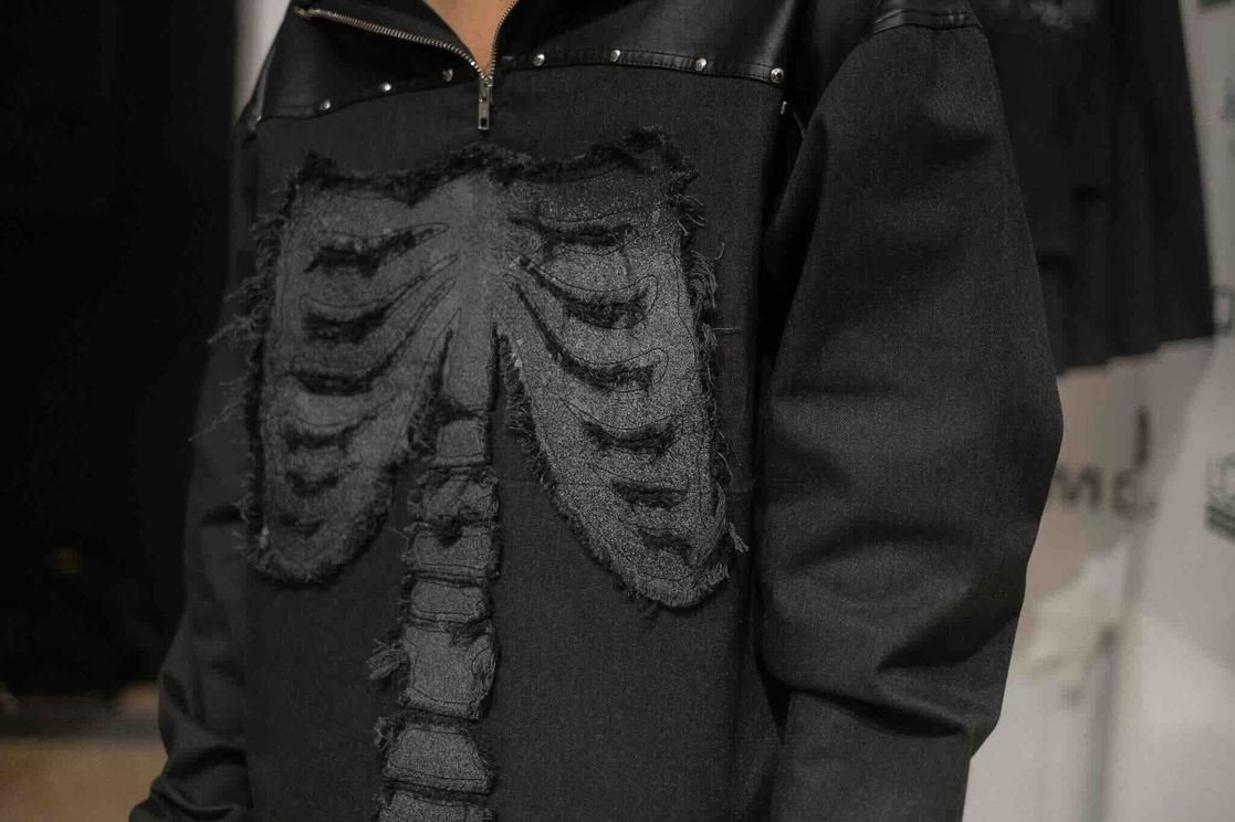 AW26 Backbone Tour runway look 3: Grey denim sweater with bones patch detail, rock-and-roll grunge styling — Duarte Hajime Lisboa Fashion Week 2026