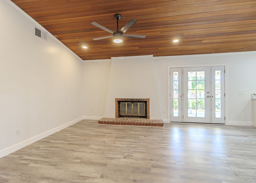 Empty living room with wooden ceiling, ceiling fan, and brick fireplace. Glass doors open to greenery. Bright, modern, and fresh ambiance.