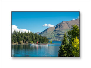 Steamship Earnslaw motors out of Queenstown on a bright sunny blue sky day with mountains in the background