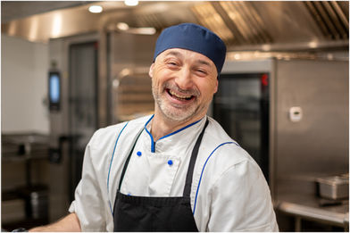 A smiling head chef looks up at the camera while cooking lunch at a rest home in Auckland