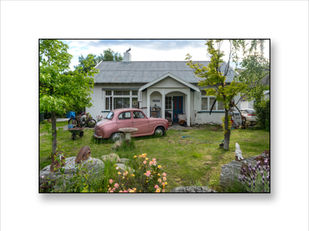 a rural New Zealand front yard with an old Austin car and a garden gnome in front of a farm house