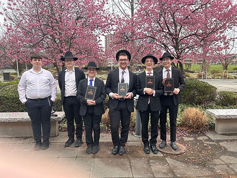 Young men in suits holding books under cherry blossoms