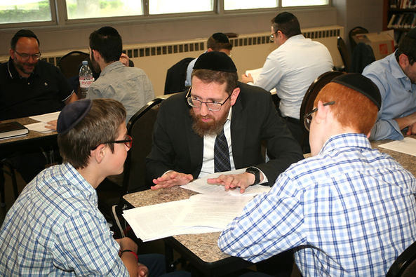 Rabbi teaching two students at a table in a Beis Midrash